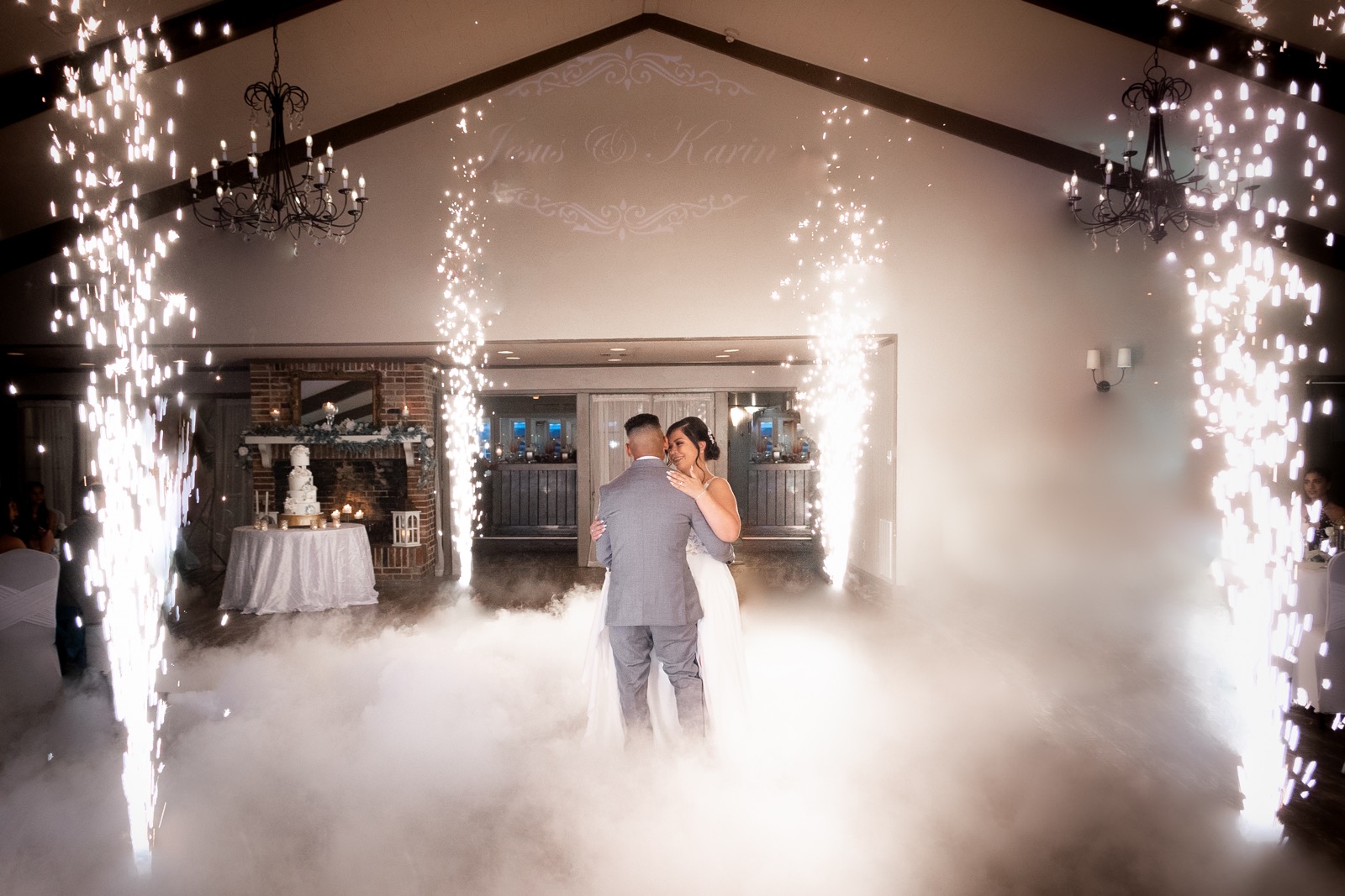 Bride and groom share a romantic first dance amid fog and sparkling fireworks in an elegant hall, creating a magical and joyous atmosphere.