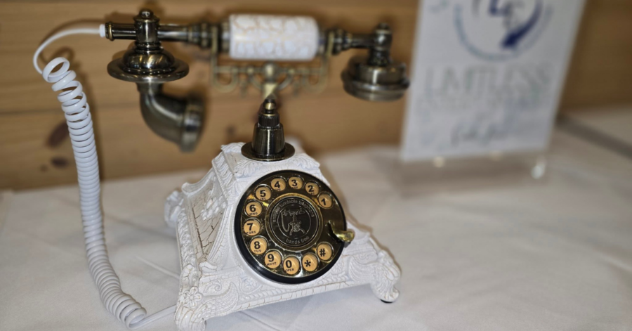 A vintage white rotary phone with ornate details is placed on a table. The phone's brass accents and coiled cord evoke a nostalgic feel.