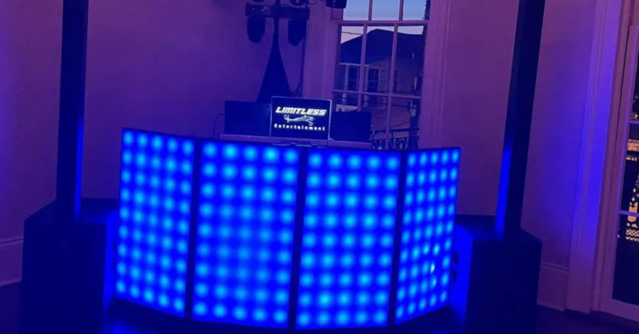 Illuminated DJ booth with glowing blue lights in a dimly lit room. A screen displays "Limitless Entertainment." Elegant atmosphere.